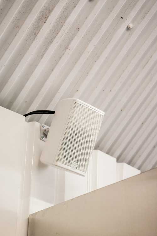 A white speaker, as part of a builtin sound system, in the top corner of a railway arch